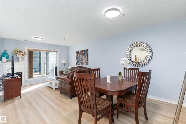 Living and dining area with light blue walls, wood-look flooring, and a brown leather sofa. - #131 16035 132 St Nw, Edmonton