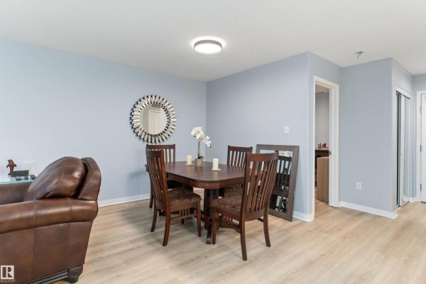 Dining area and hallway entrance with light blue walls, wood-look flooring, and a dark wood dining set. - #131 16035 132 St Nw, Edmonton