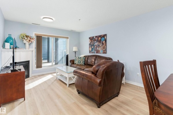Living room with a gas fireplace, brown leather sofa, white coffee table, and a sliding glass door. - #131 16035 132 St Nw, Edmonton
