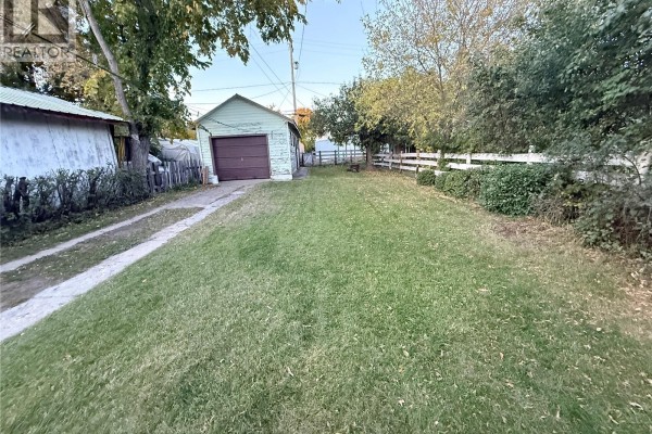 View of a large green backyard with a detached garage and white fence. - 131 2nd Avenue W, Biggar