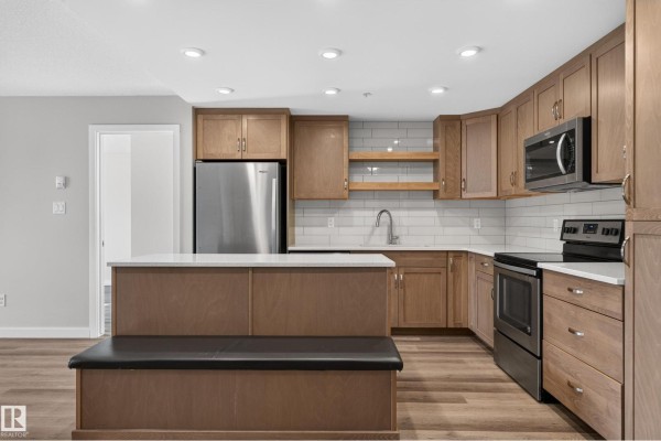 Kitchen with stainless steel refrigerator, dishwasher, sink, and light wood cabinetry against white tile. - #131 5504 Schonsee Dr Nw, Edmonton