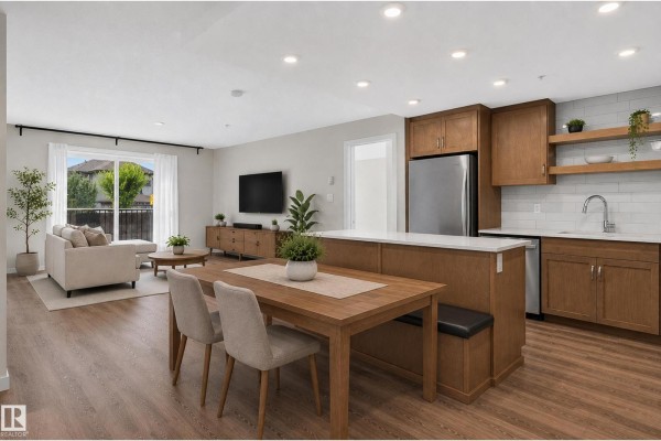 Living and dining area with furniture, facing a kitchen island with breakfast bar and a sliding glass door. - #131 5504 Schonsee Dr Nw, Edmonton