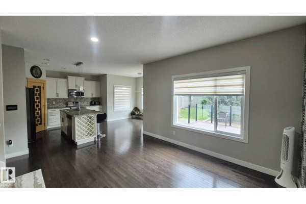 Living room with a large window overlooking the backyard, adjacent to a modern kitchen. - 131 57 St Sw, Edmonton