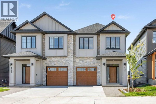 Front exterior of a modern duplex with stone and light grey siding and double garage doors. - 131 Greenwich Drive Nw, Calgary