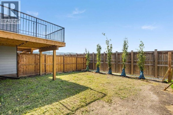 Backyard of a duplex with a wooden fence, green grass, and a raised deck. - 131 Greenwich Drive Nw, Calgary