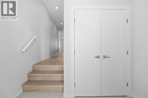 Interior hallway with stairs, light wood flooring, white double doors, and a white handrail. - 131 Greenwich Drive Nw, Calgary