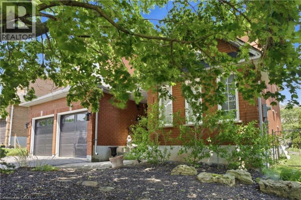 Side view of a brick house with two garage doors and landscaping under trees. - 131 Huntingwood Avenue, Hamilton