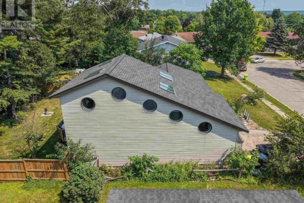 Side view of a house with horizontal beige siding and unique round windows under a dark gray roof. - 131 Meadow Park Cres, Sault Ste  Marie