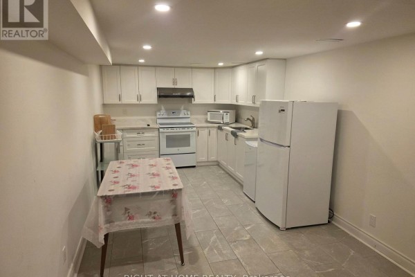 A compact white kitchen with white cabinets, appliances, a stove, and a small table. - 131 Thicketwood Drive, Toronto