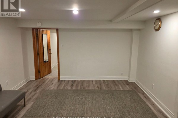 Living area with light gray laminate flooring, white walls, and a wooden sliding door. - 131 Thicketwood Drive, Toronto