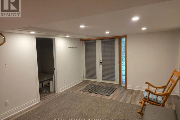 Living area with wooden rocking chair, gray sofa, French doors, and an entrance to a room. - 131 Thicketwood Drive, Toronto
