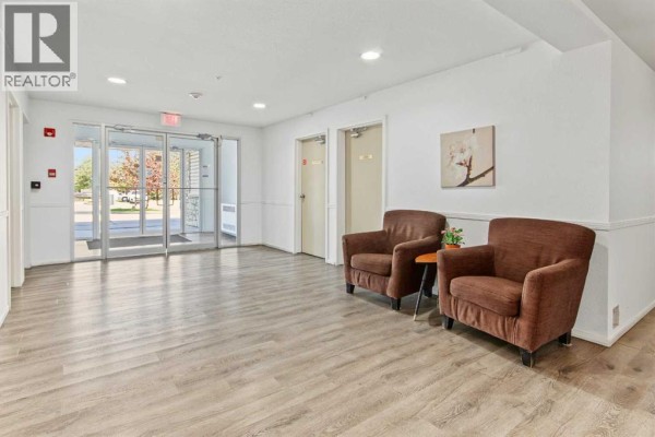 Building lobby with beige chairs, a small table, and glass doors leading outside. - 1310, 16320 24 Street Sw, Calgary