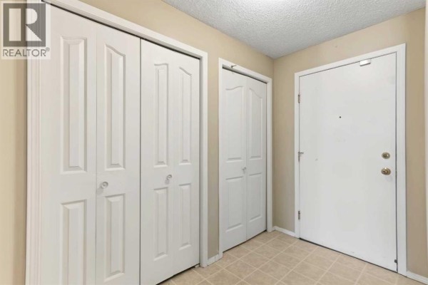 Interior hallway with beige walls, cream-colored doors, and a beige front door. - 1310, 16320 24 Street Sw, Calgary