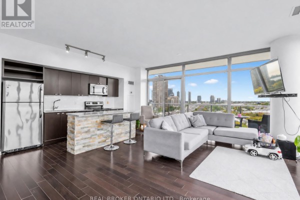 Open concept living and kitchen area with a sofa, island, stainless steel appliances, and a city view. - 1310 - 105 The Queensway, Toronto