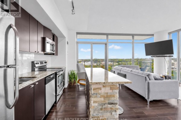 View of the kitchen island, sofa, and panoramic windows overlooking the city and lake. - 1310 - 105 The Queensway, Toronto