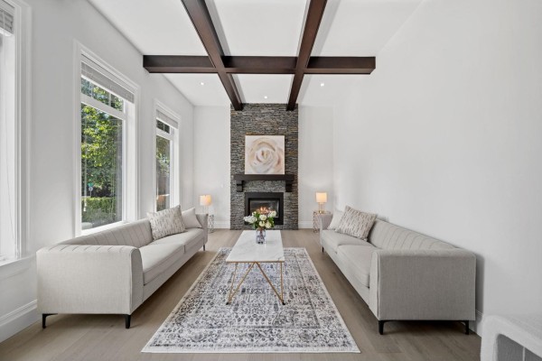 Spacious living room with a coffered ceiling, stone fireplace, and large windows overlooking trees. - 13101 14 Avenue, Surrey