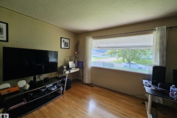 Interior room with hardwood floors, a large TV, a window with blinds, and workstations. - 13103 63 St Nw Nw, Edmonton