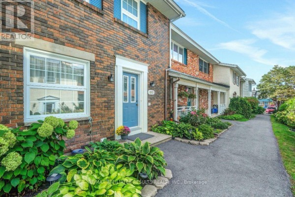 Side view of a brick townhouse exterior showing the walkway and garden beds. - 1312 Cornell Street, Ottawa
