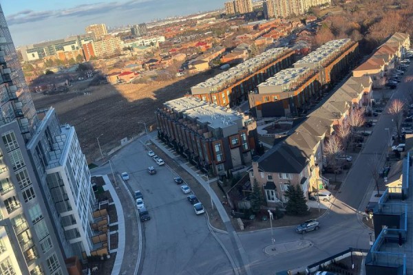 View of a street with parked cars, townhouses, and a tall glass building. - 1313 - 260 Malta Avenue, Brampton