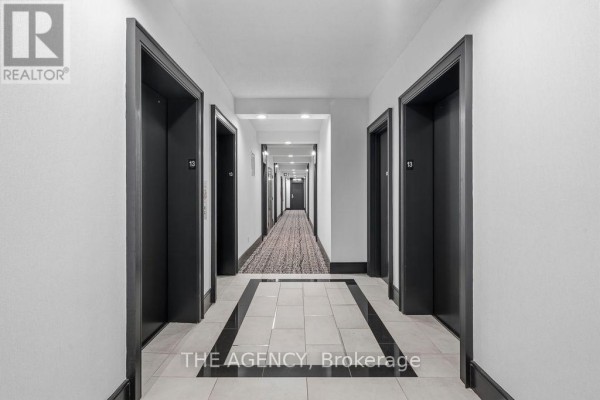 A long hotel-style hallway with multiple elevator doors and a patterned carpet. - 1314 - 438 King Street W, Toronto