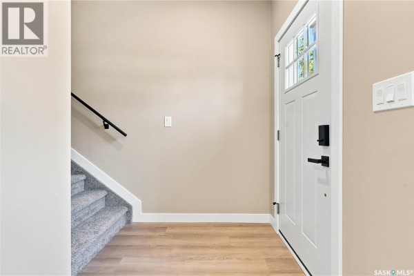 Interior view of a clean, bright foyer with a white front door, light wood floor, and carpeted stairs. - 1314 Connaught Avenue, Moose Jaw