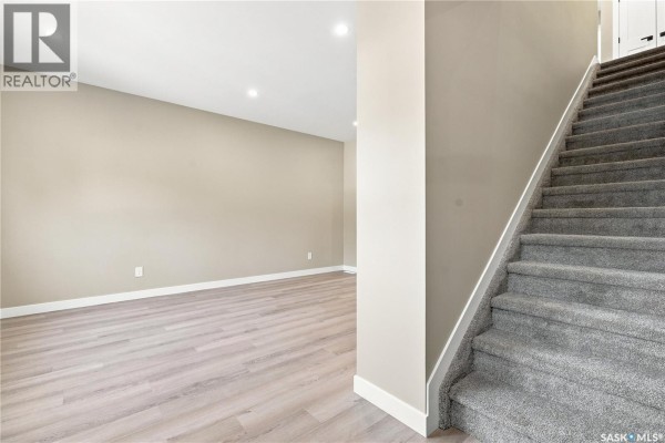 View of a carpeted staircase and adjacent room with neutral walls and light wood laminate flooring. - 1314 Connaught Avenue, Moose Jaw