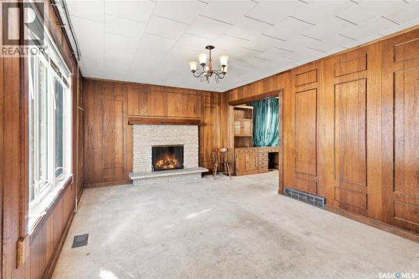 Living room with wood paneling, a stone fireplace, and a built-in bookshelf. - 1315 2nd Avenue N, Saskatoon