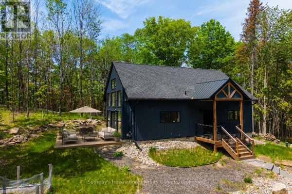 Front exterior of a dark blue house with a wooden-beam covered porch and stone landscaping. - 1315 North Drive, Dysart Et Al