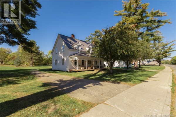Side view of a white farmhouse with a wraparound porch, surrounded by trees and grass. - 1319 Aroostook Rd., Perth Andover