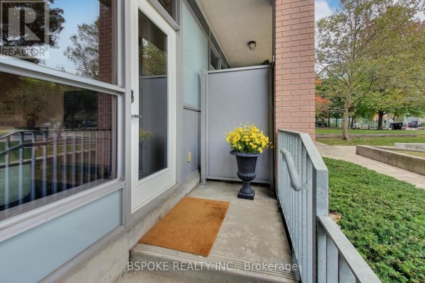 Close-up of apartment entrance with a potted yellow flower, doormat, and metal railings. - 132 - 1005 King Street W, Toronto
