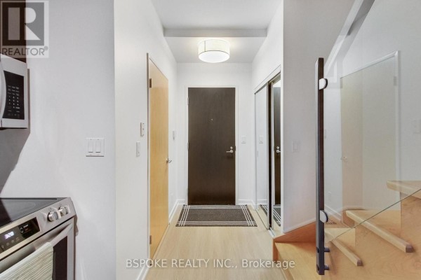 Interior hallway with dark wood door, mirrored closet, modern light fixture, and a staircase with glass railing. - 132 - 1005 King Street W, Toronto