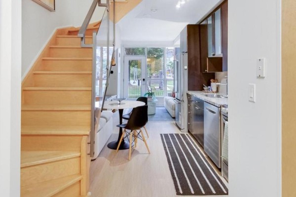 View of kitchen and dining area with stainless steel appliances, light wood stairs, and sofa visible through window. - 132 - 1005 King Street W, Toronto