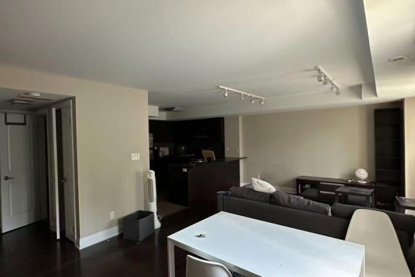 Living room and kitchen area with dark floors, a sectional sofa, dining table, and dark cabinets. - 132 - 322 John Street, Markham