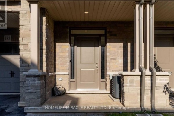 Front view of a beige brick townhouse with a grey garage door labeled 132. - 132 - 77 Diana Avenue, Brantford