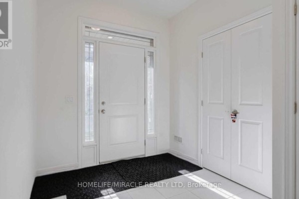 Hallway with white walls, tile flooring, a rug, and a staircase with wooden banisters. - 132 - 77 Diana Avenue, Brantford