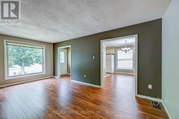 Living room with hardwood floors, large window, and doorway to kitchen area. - 132 Ardsley Crescent, London North