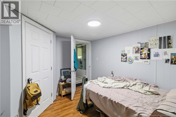 Bedroom with a bed, open door to a bathroom, and wood-paneled accent wall. - 132 Golf Club Road, Fredericton