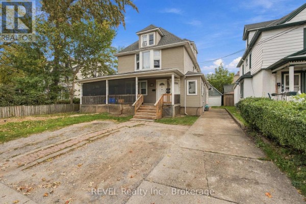 Side view of a beige two-story multi-family home showing a driveway and adjacent properties. - 132 Hellems Avenue, Welland