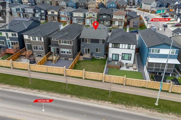 Aerial view of backyards showing fences, decks, and grass areas with a street and houses behind. - 132 Howse Crescent Ne, Calgary
