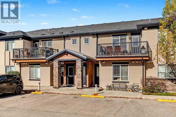 Exterior view of multi-unit townhouse complex with beige siding and dark trim under a blue sky. - 13204, 2781 Chinook Winds Drive Sw, Airdrie