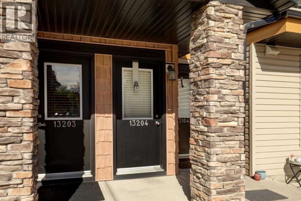 Close-up view of townhouse entrances with dark doors, stone pillars, and wood shingle accents. - 13204, 2781 Chinook Winds Drive Sw, Airdrie