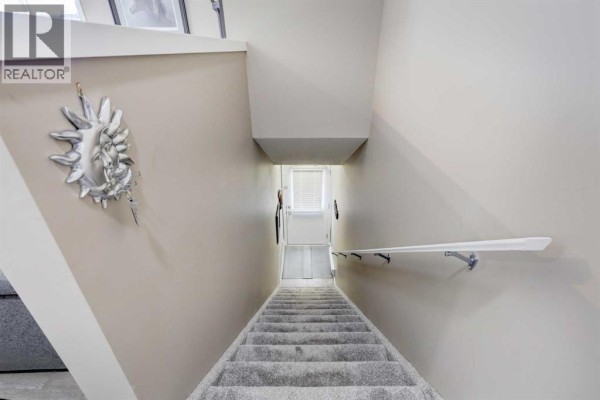Interior view looking down a carpeted staircase with beige walls and a white handrail. - 13204, 2781 Chinook Winds Drive Sw, Airdrie