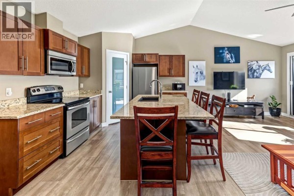 Open-concept kitchen and living area with wood cabinets, granite countertops, and vaulted ceiling. - 13204, 2781 Chinook Winds Drive Sw, Airdrie