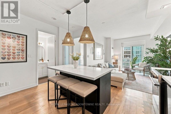 Kitchen island with pendant lights, overlooking a living area with sofa and chairs. - 1321 - 165 Legion Road N, Toronto