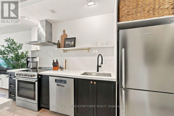 Compact kitchen with stainless steel appliances, white quartz countertops, and dark cabinetry. - 1321 - 165 Legion Road N, Toronto