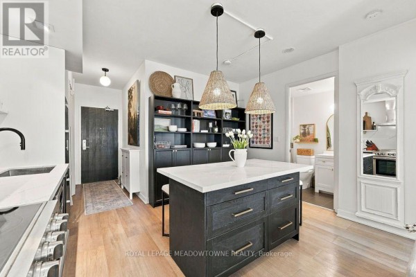 View of the apartment's open-concept kitchen, island, hallway entrance, and bathroom door. - 1321 - 165 Legion Road N, Toronto