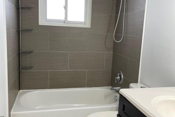 Bathroom with a white bathtub, grey tiled walls, a small window, and a vanity. - 1321 Cedar Street, Oshawa