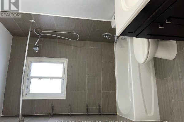 Bathroom showing a white bathtub, toilet, grey tiled walls, and a small window. - 1321 Cedar Street, Oshawa