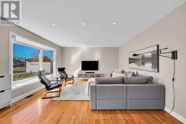 Living room with a bay window, sectional sofa, two chairs, and hardwood floors. - 1321 Rustic Drive, Ottawa