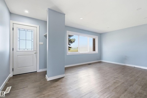 Living room with light blue walls, a large window, and gray wood-look flooring. - 13223 85 St Nw, Edmonton